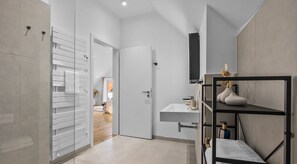 A modern bathroom with a white sink, a mirror, and a shelf with toiletries.