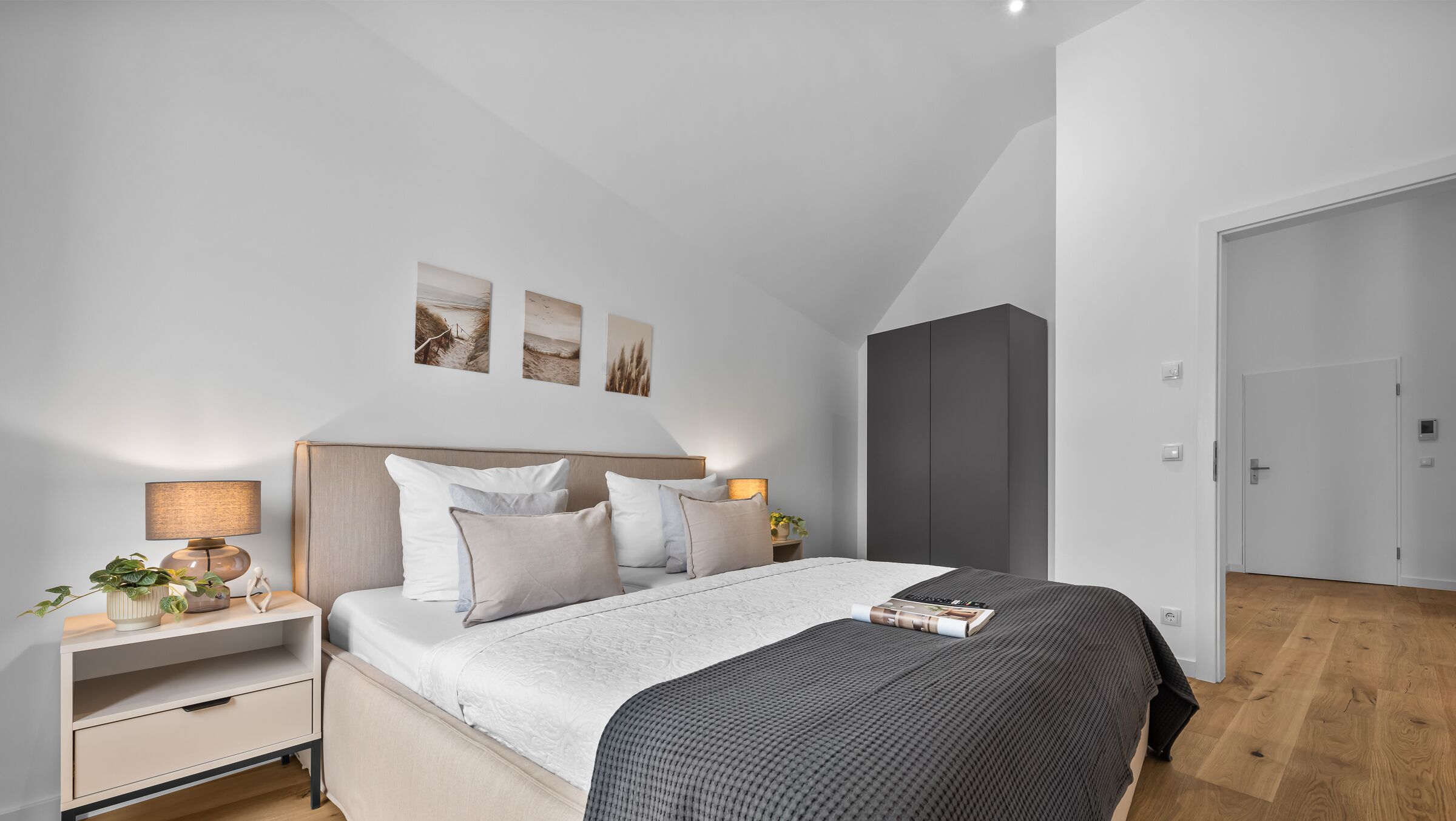 Un dormitorio moderno con una cama grande, mesitas de noche, un armario y cuadros en la pared.