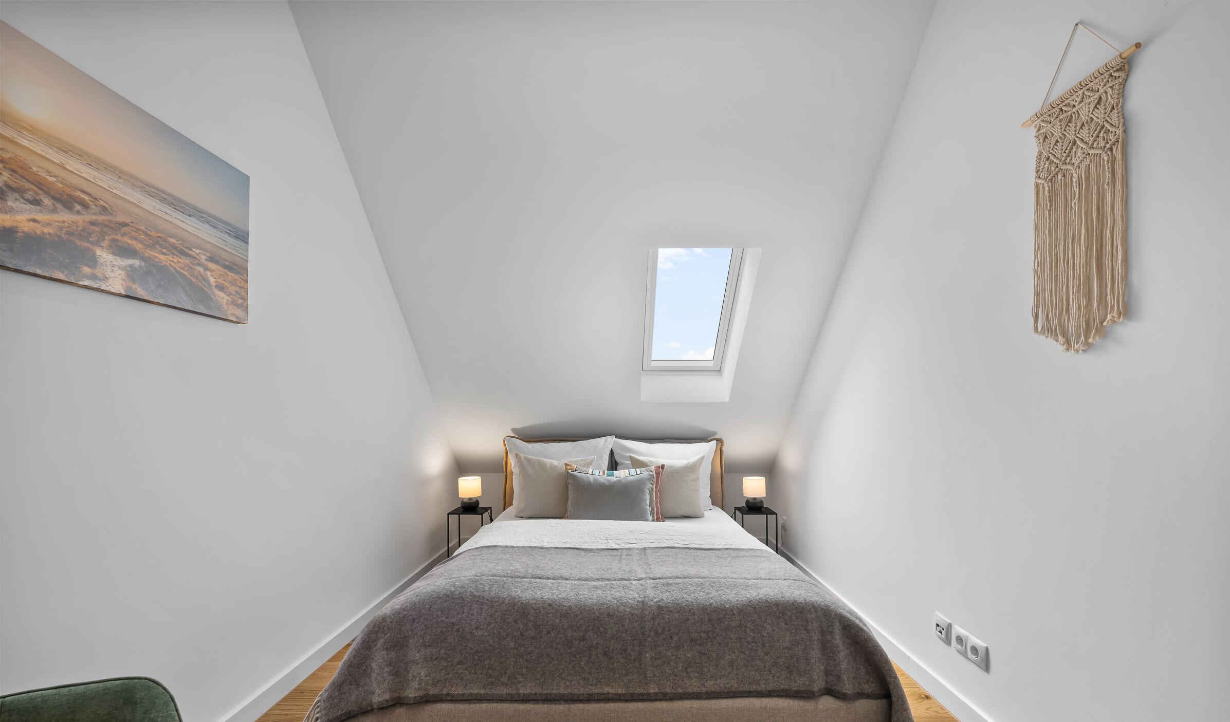 Ein Schlafzimmer mit Bett, Nachttischlampen, einem Oberlicht und einer Wandbehänge aus Makramee.