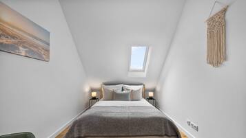 Ein Schlafzimmer mit Bett, Nachttischlampen, einem Oberlicht und einer Wandbehänge aus Makramee.