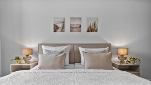 A bedroom with a large bed, two bedside tables with lamps, and three wall-mounted paintings.