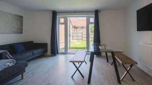 A modern living room with a sofa, a glass-top dining table, and a bench. - Stylish 3-Bed Retreat with Garden and Parking (Woodford Halse)