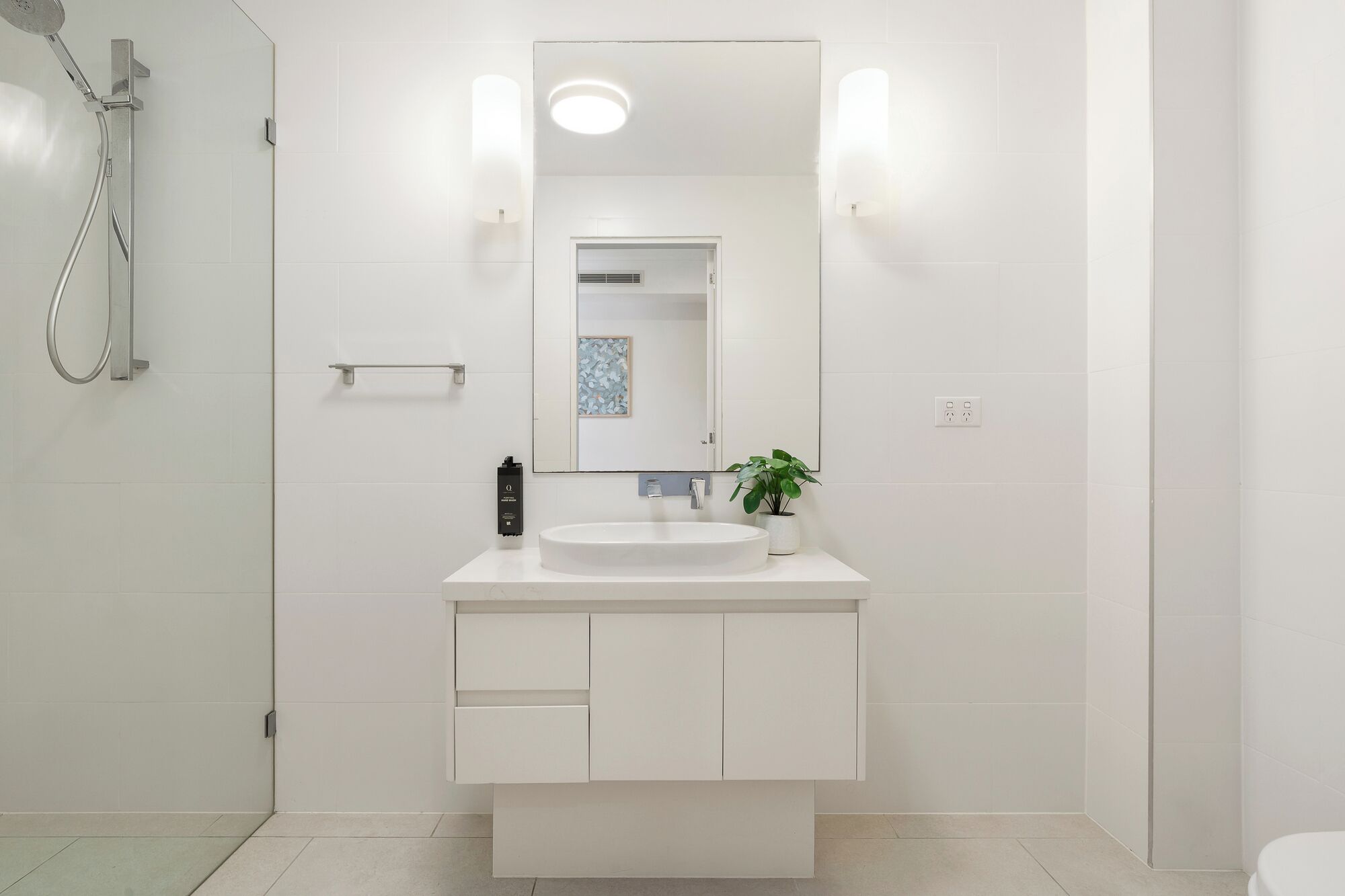 A modern bathroom with a white sink, mirror, and shower.