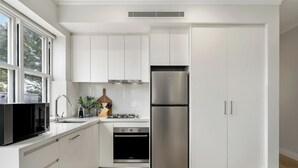 A modern kitchen with white cabinetry, a double-door refrigerator, a built-in oven, and a microwave. - Urban Rest Double Bay Beach (Double Bay)