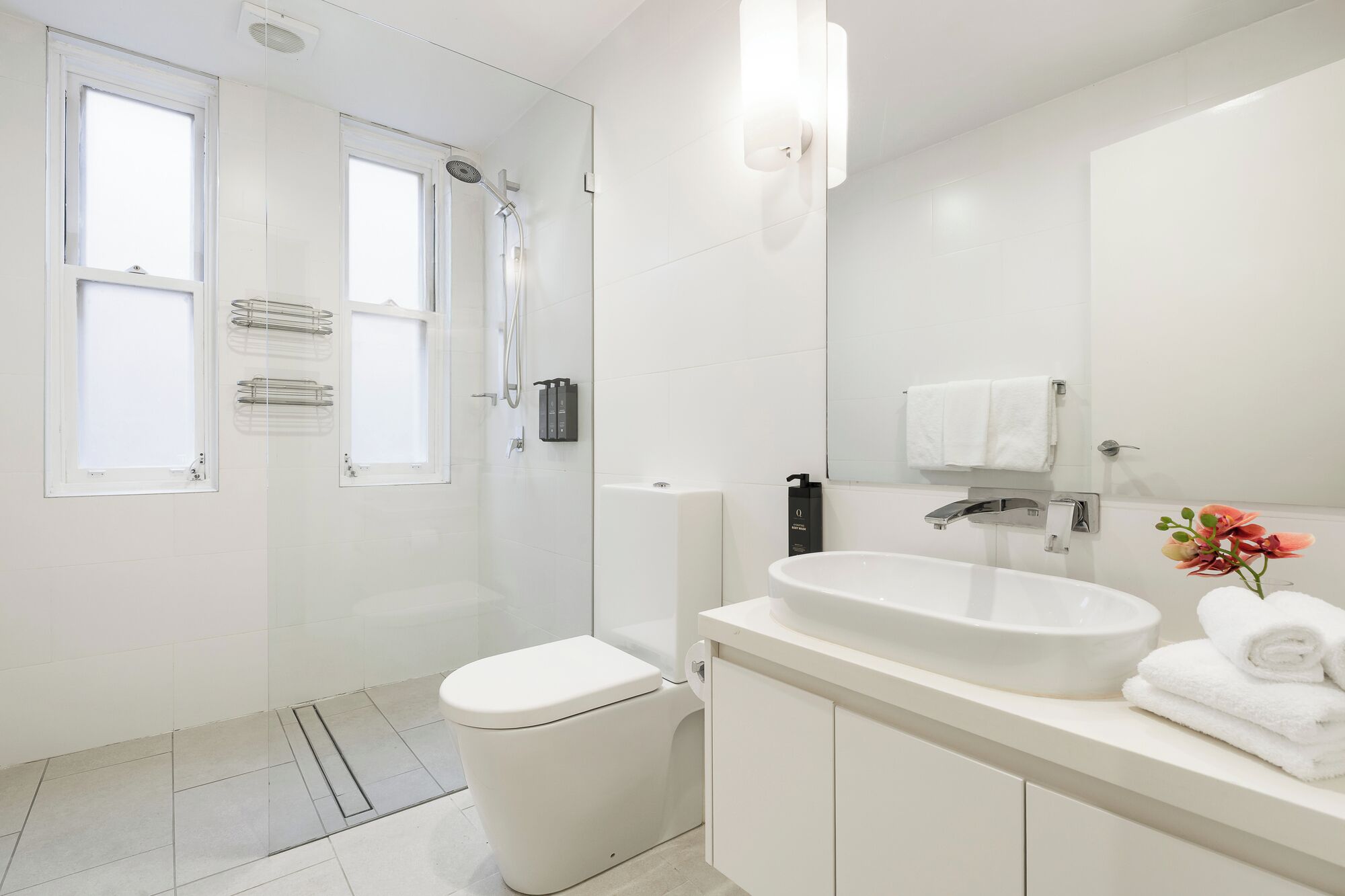 A modern bathroom with a shower, toilet, sink, and a large mirror.