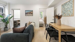 A modern living room with a sofa, a dining table with chairs, a painting, and a potted plant. - Urban Rest Double Bay Beach (Double Bay)