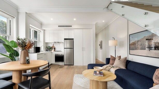 A modern kitchen with white cabinets, a stainless steel refrigerator, and a dining area with a round table and chairs. - Urban Rest Double Bay Beach (Double Bay)