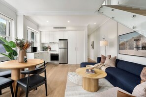 A modern kitchen with white cabinets, a stainless steel refrigerator, and a dining area with a round table and chairs.