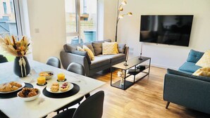 A modern living room with a dining area, grey sofas, a flat-screen TV, and a wooden floor.