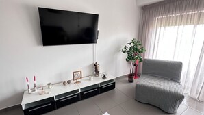 En moderne stue med et fladskærms-tv på væggen, en grå sofa, et hvidt konsolbord med pynteting og en potteplante.