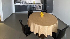 Et moderne spiseområde med et rundt bord, sorte stole og et køkken i baggrunden.