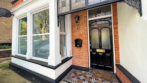 Un bâtiment traditionnel avec une porte noire, une fenêtre à cadre blanc et un porche carrelé.
