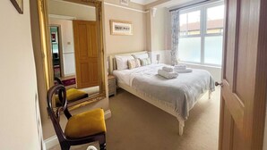 Une chambre d’hôtel avec un grand lit, une chaise en bois, un miroir, un lustre et une fenêtre donnant sur un beau paysage.
