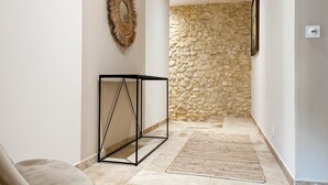 Un couloir avec un mur en pierre, un miroir à motifs tissés, un présentoir en métal noir et un tapis tissé.