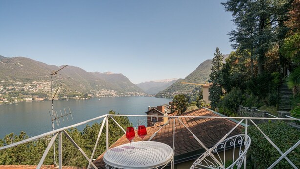 A terrace with a metal chair and table, overlooking a lake and mountains.