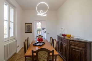A dining room with a wooden table, chairs, a radiator, a window, and a kitchen area with cabinets and a countertop.
