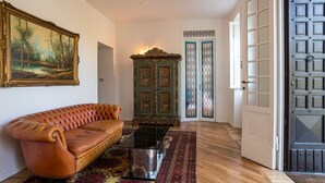 A room with a leather sofa, a glass coffee table, a patterned rug, a painting, a wooden cabinet, and a door with glass panels.