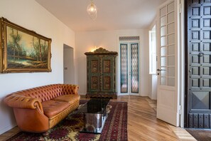 A room with a leather sofa, a glass coffee table, a patterned rug, a painting, a wooden cabinet, and a door with glass panels.