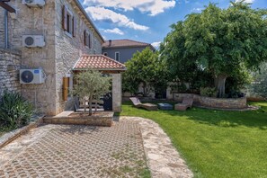 A stone building with a tiled roof, a paved courtyard, and a large tree. - Casa Rustica Felker With Private Pool (Marcana)