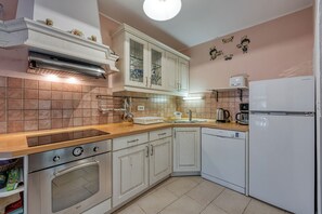 Una cocina con gabinetes blancos, horno empotrado, cafetera y lavavajillas.