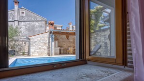 A view from a window of a stone building with a pool, stone walls, and a clear blue sky. - Casa Rustica Felker With Private Pool (Marcana)