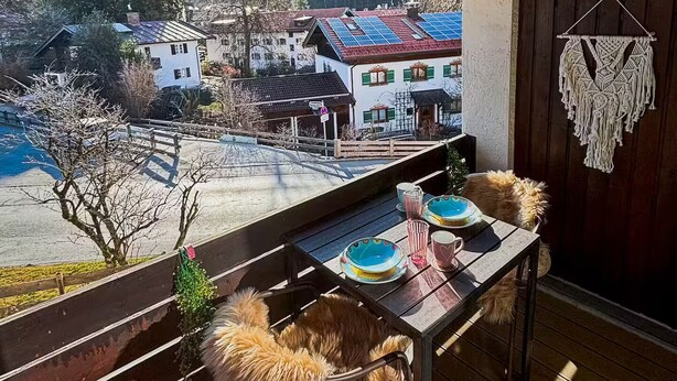 Een balkon met een tafel gedekt voor twee personen, met uitzicht op een dorp met huizen en een berg op de achtergrond.