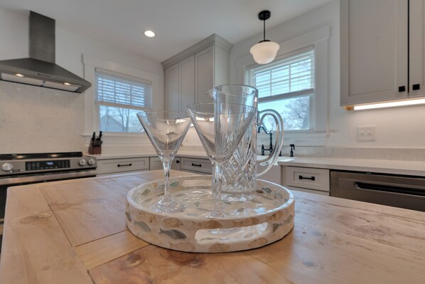 A kitchen with white cabinets, a stainless steel range hood, and a wooden island with a glass pitcher and two wine glasses.