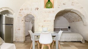 Habitación compacta con cama, una mesa de comedor con sillas, un refrigerador y una botella verde en un nicho.