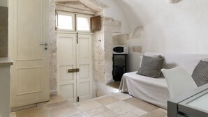 Una habitación con una puerta blanca, un sofá blanco, un microondas y una pared de piedra.