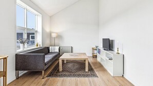 Una sala de estar moderna con sofá, mesa de centro y mueble para televisión, con un ventanal grande y radiador.