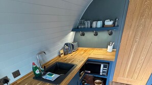 A compact kitchen with a wooden countertop, a built-in stove, and a sink. - Lotus Pod Self-Catering glamping in Suffolk (Henley)