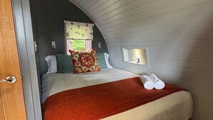A cozy bedroom with a curved ceiling, a bed with white linens, a red throw blanket, and two pillows. - Lotus Pod Self-Catering glamping in Suffolk (Henley)