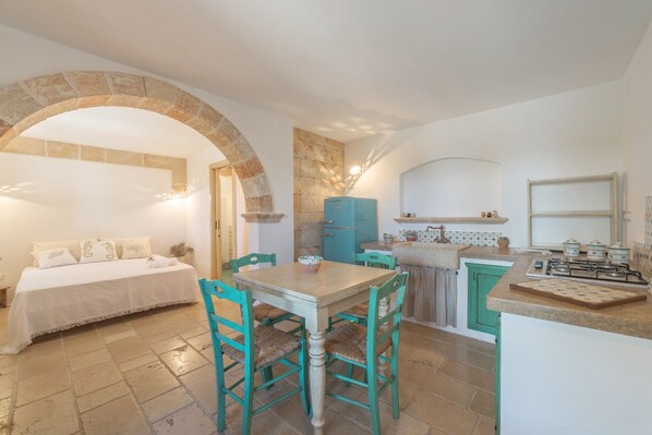 Una habitación acogedora con una cama, una mesa de comedor y sillas, una zona de cocina con estufa y un arco de piedra.