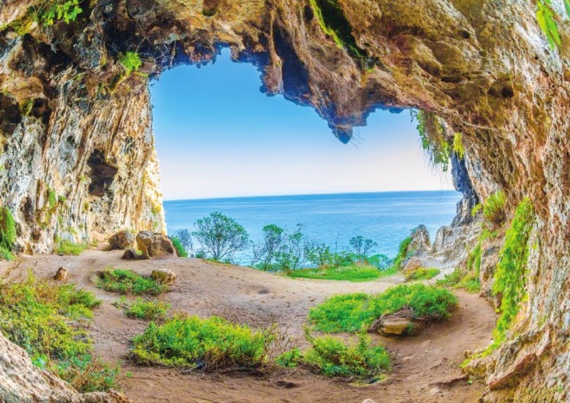 A natural cave opening with a view of the sea and a dirt path leading through it.