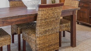 A dining area with a wooden table, wicker chairs, a white decorative bowl, and a wooden cabinet. - Villetta Sulvia - Alloggio Alaterno con Terrazza Vista Mare (Corsano)