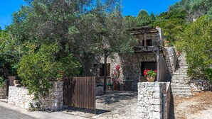 A stone building with a wooden gate, surrounded by trees and greenery. - Villetta Sulvia - Alloggio Alaterno con Terrazza Vista Mare (Corsano)