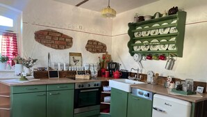 Une cuisine avec des meubles de rangement verts, un mur en briques, une étagère suspendue où sont posées des assiettes et une machine à café.