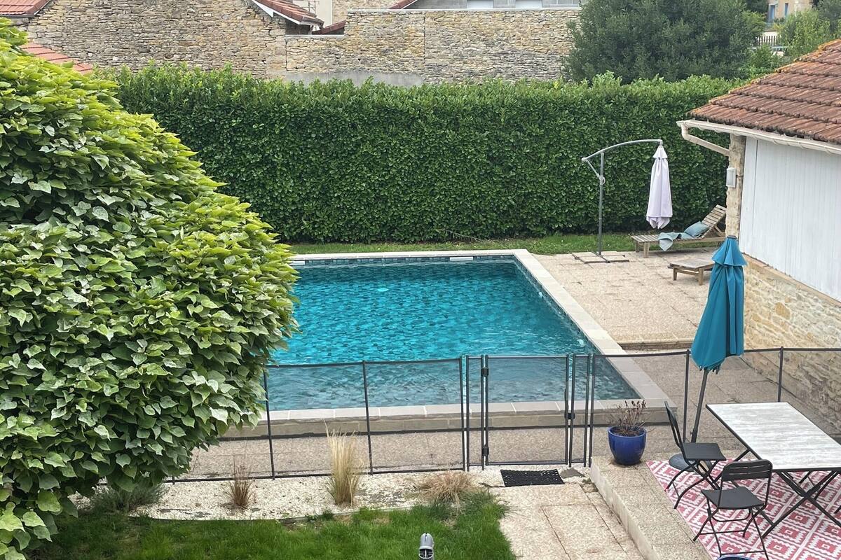 A swimming pool with a stone wall and a hedge in the foreground.