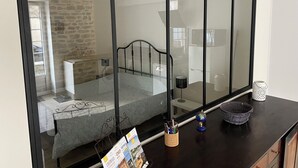 A bedroom with a glass partition, a bed, a bedside table, a lamp, and a small globe.