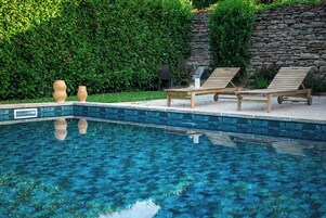 Piscina com duas espreguiçadeiras e dois vasos decorativos na borda.