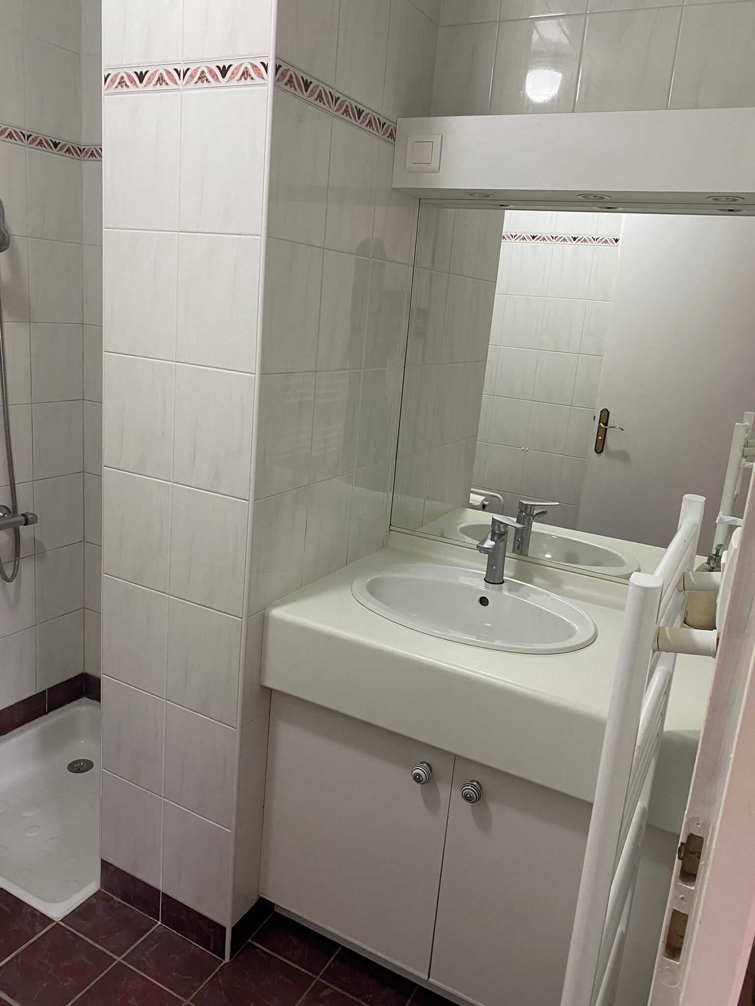 Une salle de bain avec des carreaux blancs, un lavabo, un miroir et une douche.