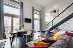 A modern living room with a dining area, large windows, a staircase, and a flat-screen TV. - Apartments with balcony near center (Prague)