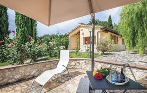 Relax in the shaded patio area with a comfortable lounge chair, a table, and a beautiful flower arrangement.