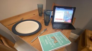 Ett träbord med en bärbar dator, en bok med titeln ”Cambridgeguiden – det du inte får missa”, en tallrik, en gaffel och ett glas.
