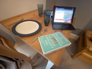 Una mesa de madera con una computadora portátil, un libro titulado 'The Cambridge Guide to What You Shouldn't Miss', un plato, un tenedor y un vaso.