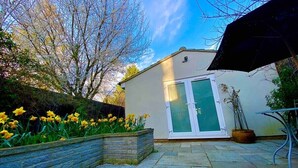 A patio area with a stone floor, a white building with a glass door, and yellow daffodils in a planter.