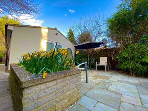 A patio area with a stone planter, outdoor furniture, and a building in the background. - Beautiful, annex, 10min from Cambridge centre (Great Shelford)