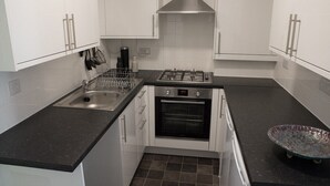 A compact kitchen with white cabinets, a stainless steel sink, a gas stove, and a built-in oven.