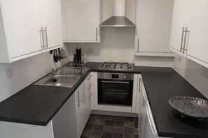 A compact kitchen with white cabinets, a stainless steel sink, a gas stove, and a built-in oven.