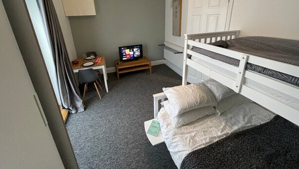 A small, neatly arranged bedroom with a bunk bed, a desk with a chair, a television, and a radiator.